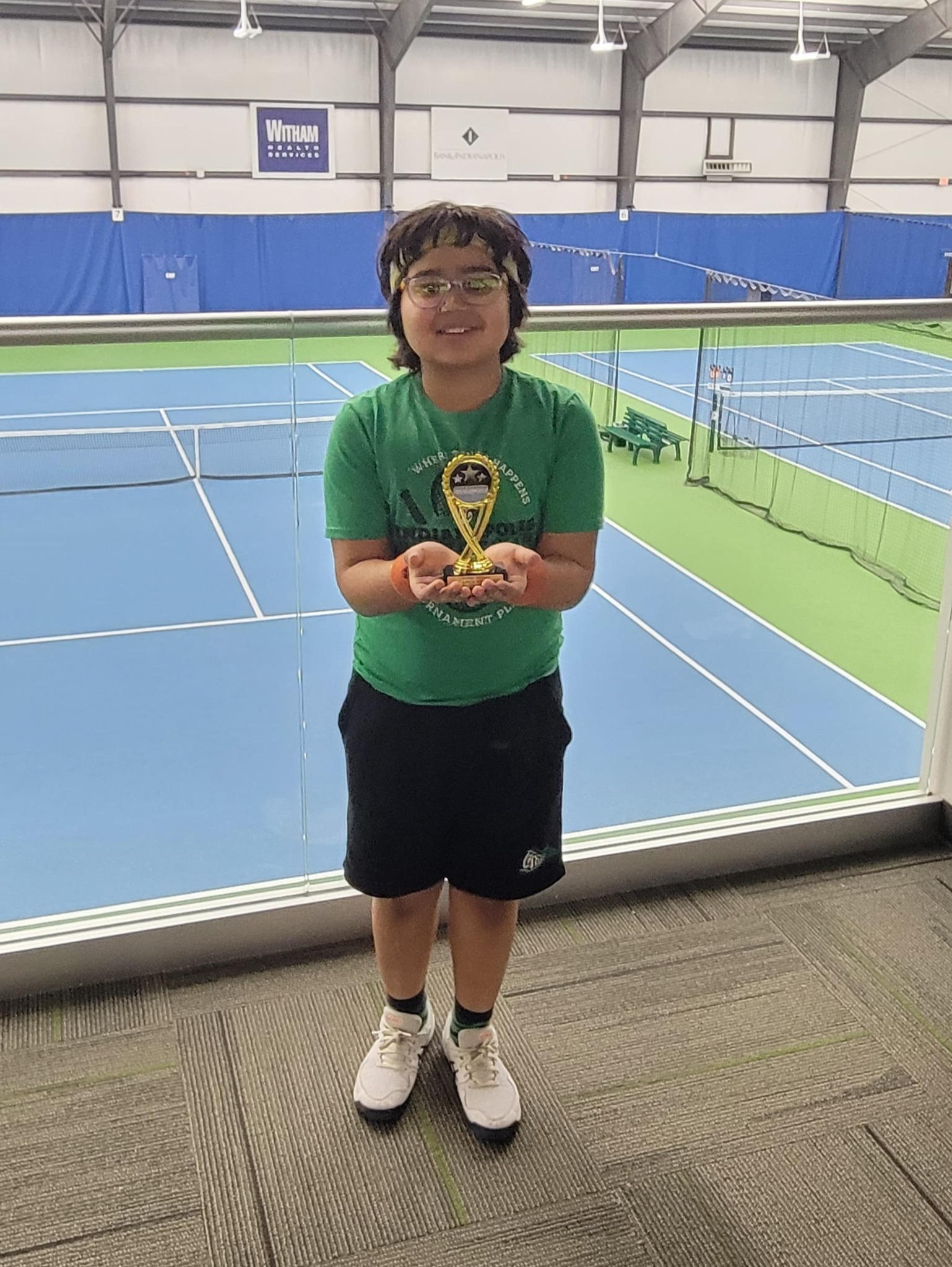 Aashil Hassija holding his tennis trophy at an indoor tennis facility